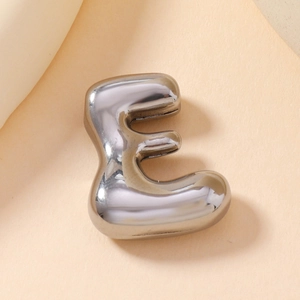 Macro shot of silver letter E pendant with cubic zirconia inlay on polished metal