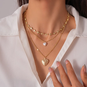 Detail of triple-layer gold necklace featuring heart pendants and pearl accents