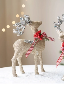 Close-up of glittery gold reindeer with red berries and bow on snowy base