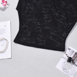 Détail d'un haut en dentelle noire avec motifs floraux et accessoires de luxe