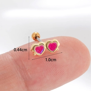 Pink double heart cartilage stud earrings in gold finish on fingertip to show scale