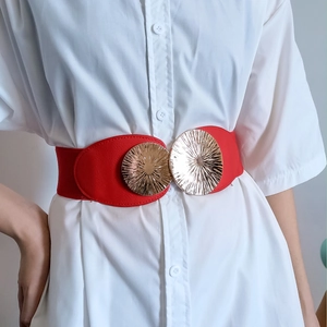 Close-up of red elastic belt with textured gold double round metal buckles on white shirt