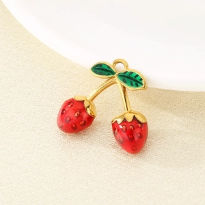 Macro shot of gold strawberry pendant with red enamel and green leaves on beige fabric