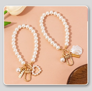 Detail of heart and shell pearl charms on gold-tone keychains for bags and phones
