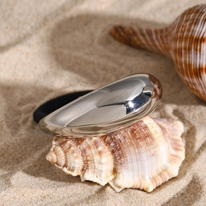 Silver teardrop stainless steel hair tie placed on a seashell at the beach