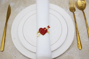 Macro view of gold heart and arrow napkin ring with red rhinestones on white cloth