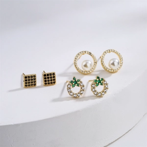 Three pairs of gold-plated earrings with pearls and colorful zircons on a white pedestal