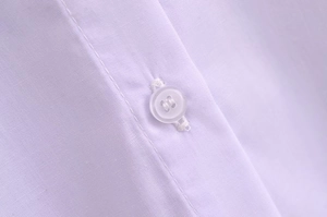Detailed close-up of clear four-hole buttons and high-quality white woven fabric texture