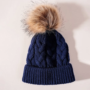 Detail view of navy blue cable knit winter hat with a brown faux fur pom pom
