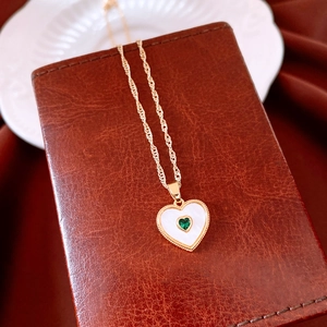 Detail of gold heart pendant necklace featuring mother of pearl and green gemstone