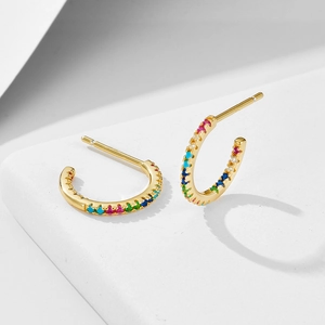 Close-up of golden C-shaped hoop earrings with rainbow pavé cubic zirconia stones