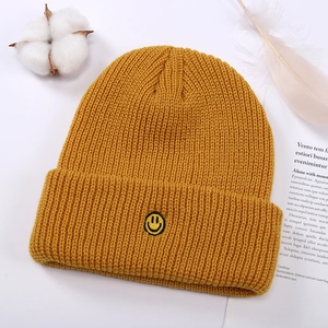 Primer plano del gorro de punto amarillo mostaza con un parche de cara sonriente bordado