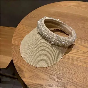 Close-up of elegant straw sun hat featuring dense pearl embellishments on the headband