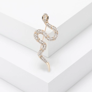 Detailed view of a gold-toned snake brooch with shimmering white rhinestones on a white stand
