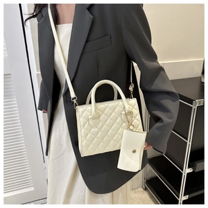 White quilted crossbody bag with matching mini purse charm held by a model in a gray suit
