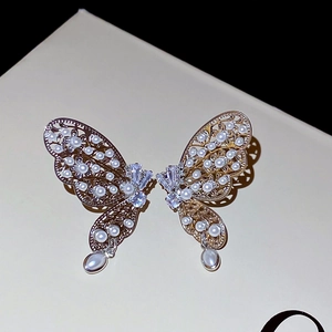 Détail de clips d'oreilles papillon avec ailes en métal évidé, perles et zircons fins