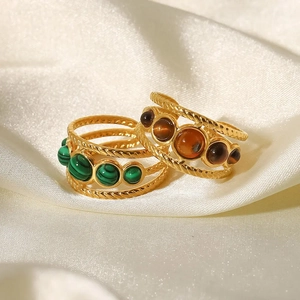 Anelli dorati vintage con malachite verde e ambra marrone su sfondo di seta bianca