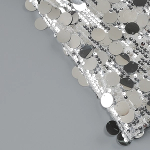 Macro detail of large silver circular sequins on white mesh fabric for evening dress