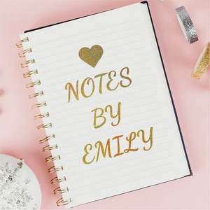 Detail of custom gold glitter letters and heart on a pink spiral notebook cover