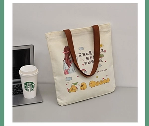 Detail of canvas tote bag with cartoon chick print and brown straps on a desktop