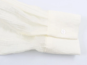 Detailed close-up of a white textured shirt cuff featuring a single button and soft pleats