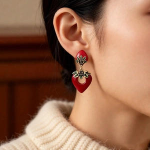 Close-up of vintage heart earrings with red enamel and gold leaf details on a model