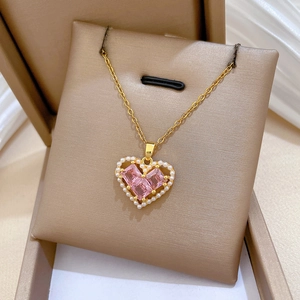 Macro detail of gold heart necklace featuring pink rectangular gems and white pearls