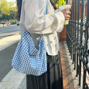 Close-up of blue and white checkered canvas tote bag worn by a model in outdoor light