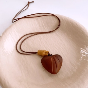 Détail d'un collier pendentif cœur en bois brun sur une assiette en céramique beige