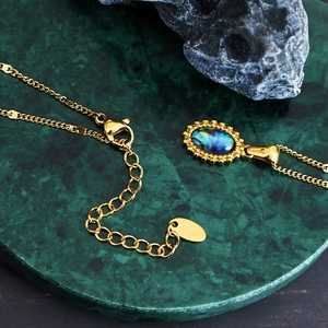Bohemian gold oval pendant necklace with colorful abalone shell on marble background
