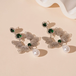 Detailed shot of butterfly earrings with green rhinestones and a white pearl drop pendant