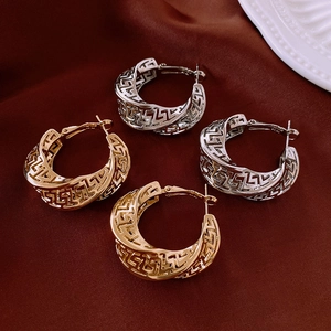 Macro detail of gold and silver Greek Key hollow hoop earrings on red silk background