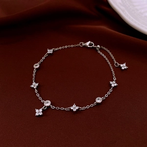 Detail of silver clover bracelet with sparkling zircons on elegant burgundy silk