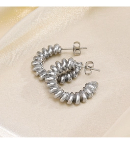 Gros plan de boucles d'oreilles créoles argentées torsadées sur du tissu en soie