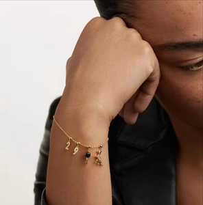 Detail of gold chain bracelet with sparkling number pendants and a blue stone key charm