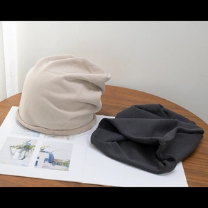 Beige and dark grey slouchy knitted beanies in a cozy minimalist aesthetic setting