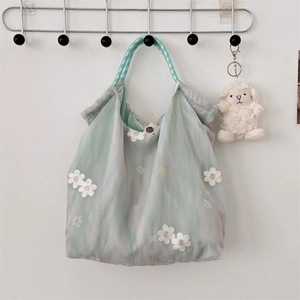 Detail of light green tulle tote bag with white floral embroidery and striped strap