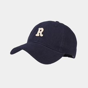 Dettaglio della lettera R color crema ricamata su un berretto da baseball in blu navy