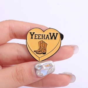 Heart-shaped Yeehaw enamel pin with cowboy boots design held in hand for display