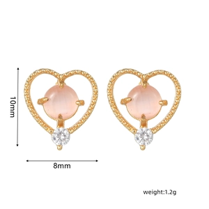 Detalle de pendientes de corazón dorados con piedra rosa y pequeño circón blanco