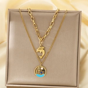 Gros plan sur collier double rang doré avec pendentifs dauphin et palmier de plage