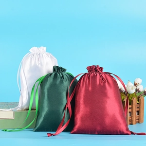 Detailed view of white, green, and red satin drawstring gift bags with silk-like luster