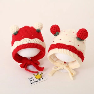 Detail van gebreide babymuts met pompons en winddichte bandjes in rood en beige