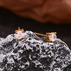 Macro shot of gold stud earrings with round-cut clear zircon on a textured stone base