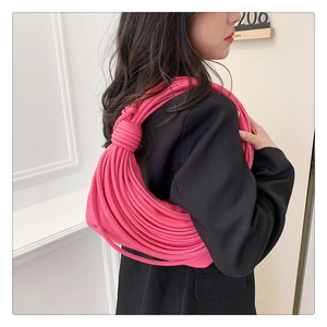 Detail view of fuchsia knot-handle shoulder bag worn by model with dark suit background
