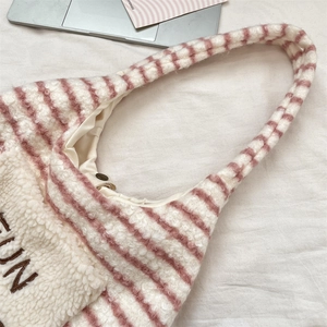 Makroaufnahme der gestreiften Plüschtasche mit rosa Lammwolltextur und Metalldruckknopf