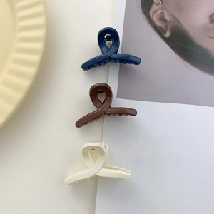 Close-up of three mini matte hair clips in navy, brown, and beige with cross twist design