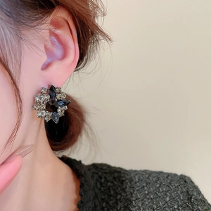Close-up of a floral rhinestone earring featuring dark grey crystals on a model's ear