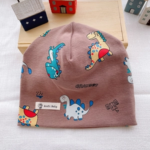 Detail of baby cotton beanie with dinosaur prints on warm wood and fabric background