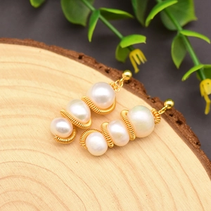 Elegant natural pearl drop earrings with handmade gold wire wrapping on a wooden base